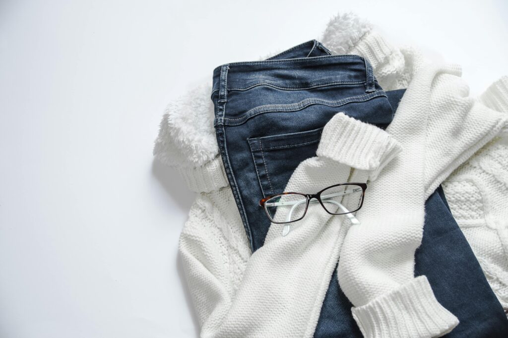 Stylish flat lay featuring Styling jeans Casual Chic, white sweater, and eyeglasses on a bright background.